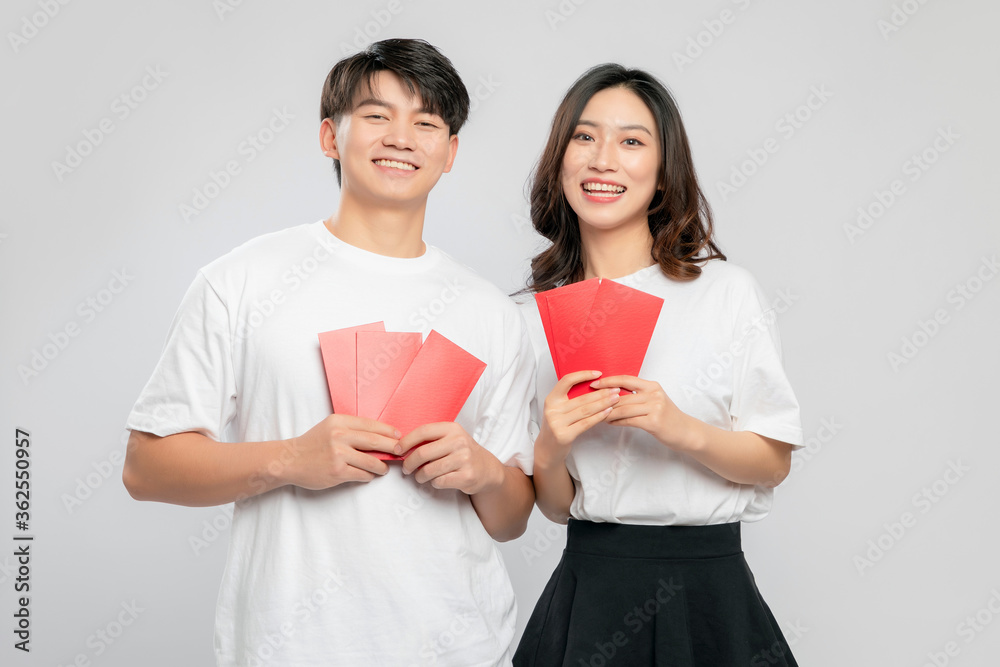 Young Asian lovers with red envelopes on New Years day in gray background

