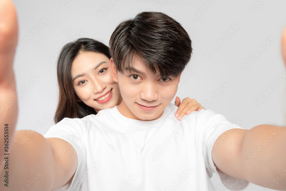 Young Asian lovers taking selfies against a gray background

