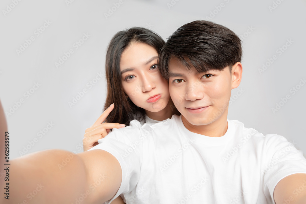 Young Asian lovers taking selfies against a gray background

