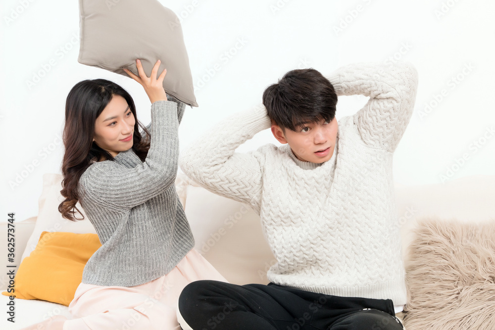 In winter, a pair of happy young Asian lovers are sitting on the sofa. The girl is beating the boy w