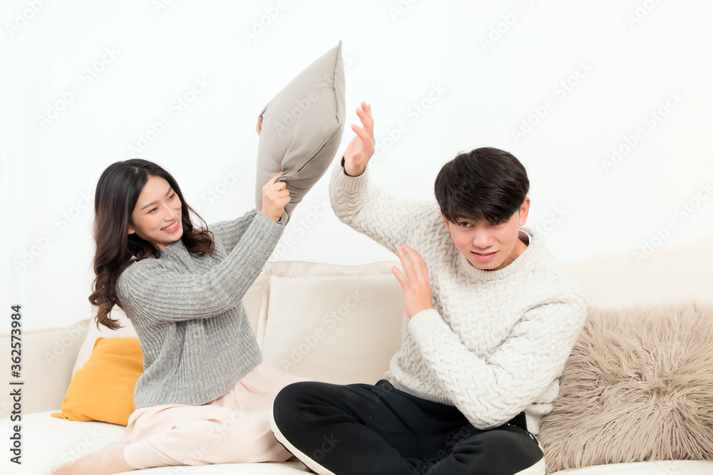 In winter, a pair of happy young Asian lovers are sitting on the sofa. The girl is beating the boy w