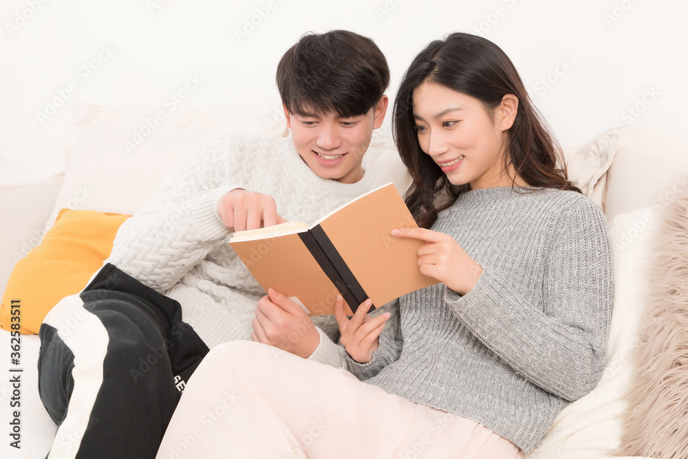 In winter, a young asian couple are reading on the sofa

