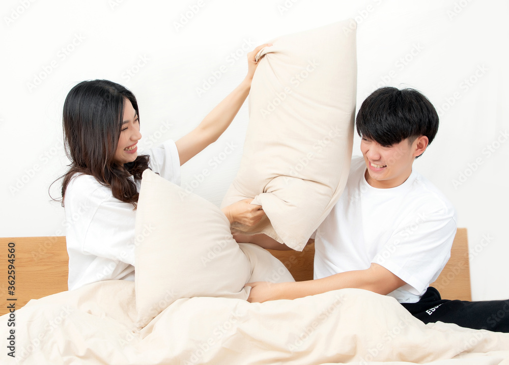 A young asian couple are sitting on the bed playing with pillows. They are very happy

