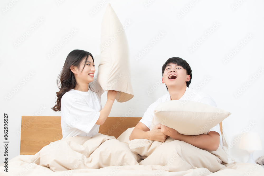 A young asian couple are sitting on the bed playing with pillows. They are very happy

