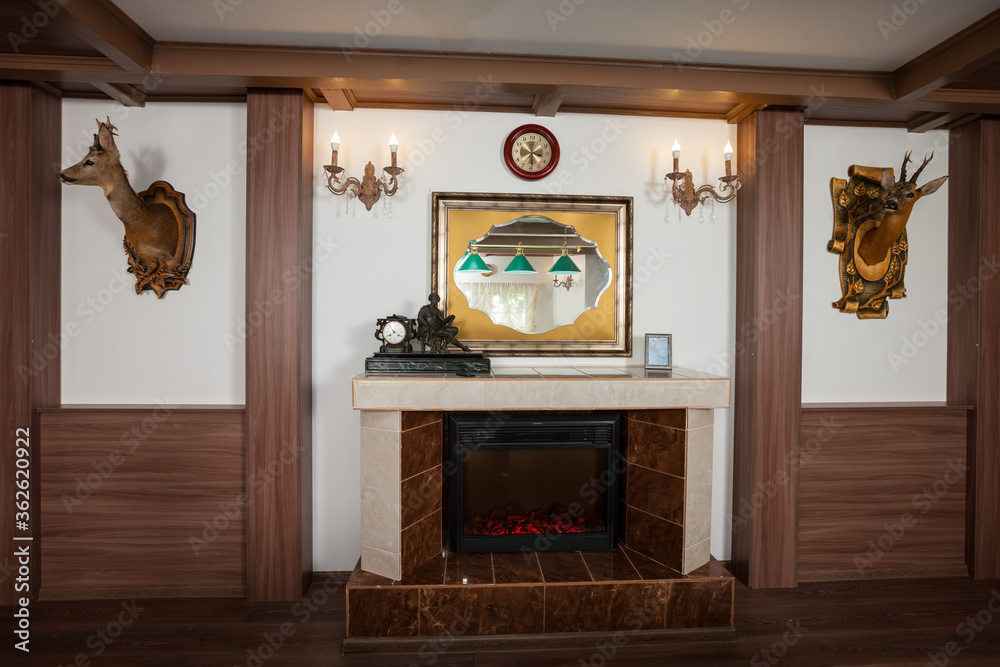 Electrical artificial fireplace in billiard room. Green lamps in the mirror. Brown wooden decor on t