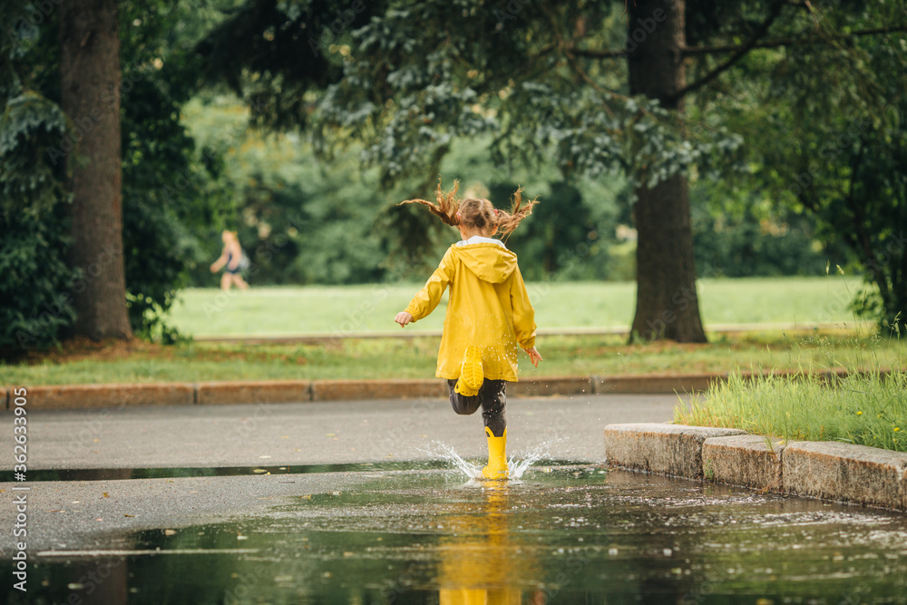 A girl in a yellow jacket and boots runs and jumps through puddles