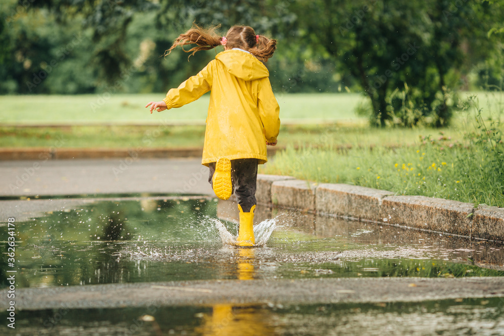 A girl in a yellow jacket and boots runs and jumps through puddles