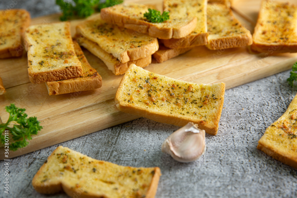 Wooden cutting board with delicious homemade garlic bread on the cement floor