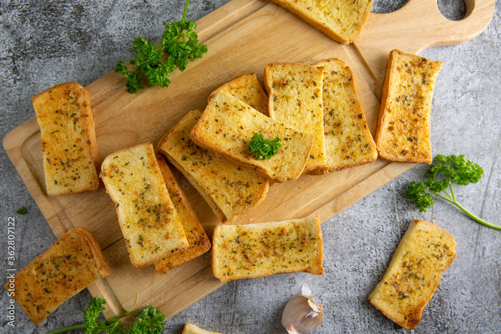 Wooden cutting board with delicious homemade garlic bread on the cement floor