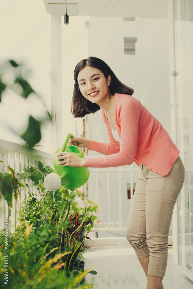 快乐的年轻亚洲女性家庭主妇在阳台上浇花