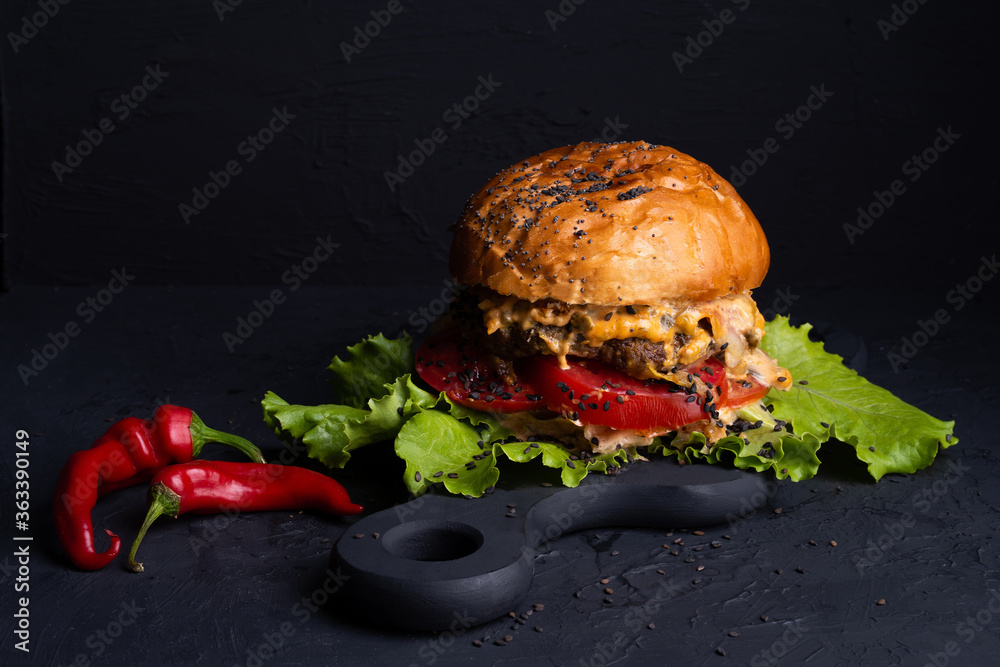 burger with spicy sauce on  black background, large and hearty sprinkled with sesame seeds, red hot 