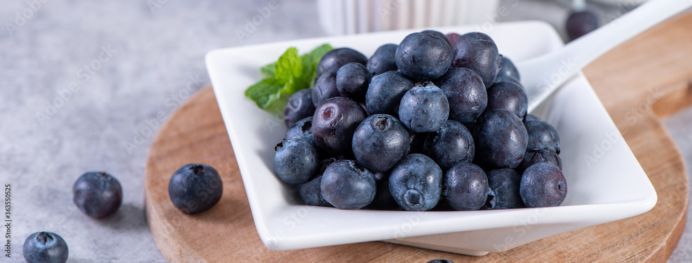 Pile of blueberry fruit in a bowl plate on a tray over gray cement concrete background, close up, he