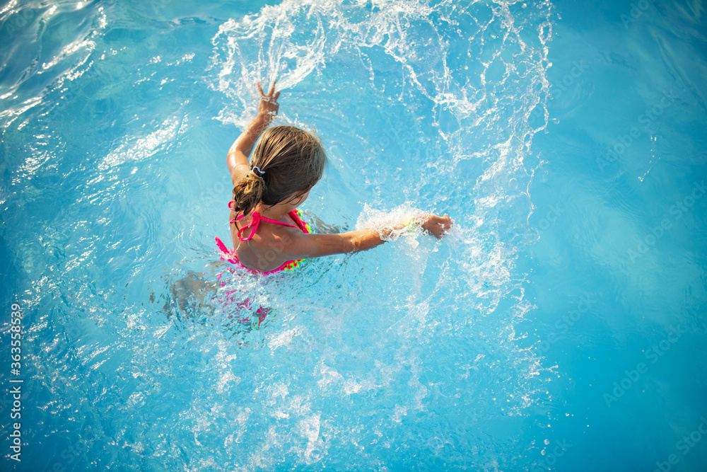 Top view happy little girl in bright color swimwear swims in the clear warm pool water Sunny summer 