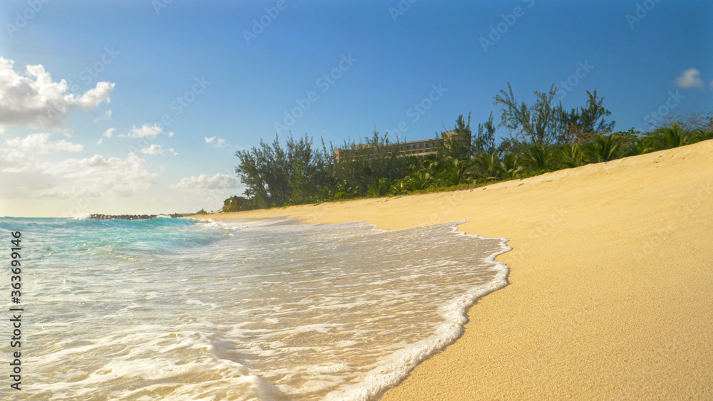 LOW ANGLE: Glassy ocean waves wash the white sand beach on a sunny evening.