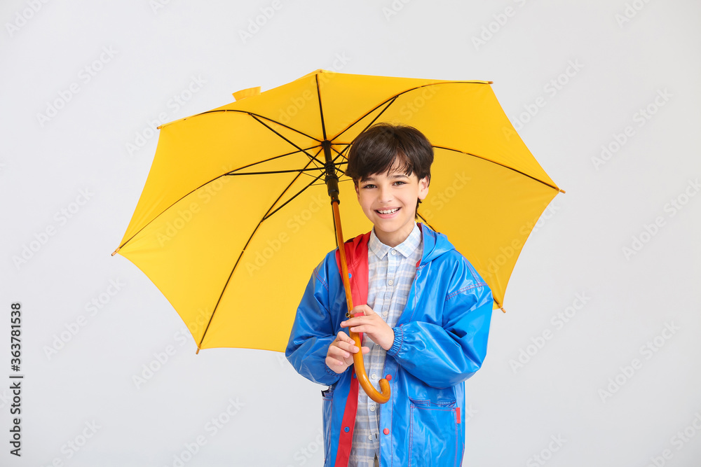 穿着雨衣，浅色背景带伞的可爱小男孩