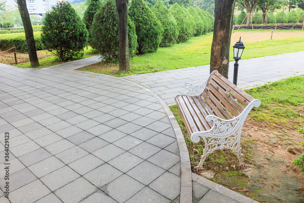 View of green garden with a small square and wooden bench for resing in the corner of the city park