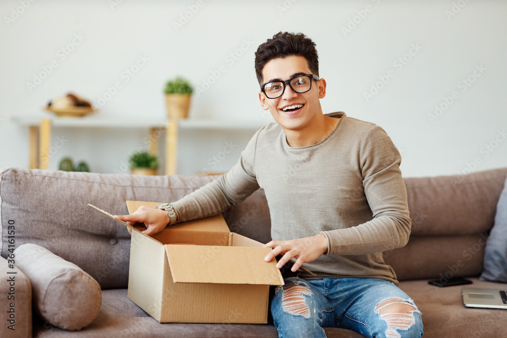 Happy man unpacking delivery box on sofa.