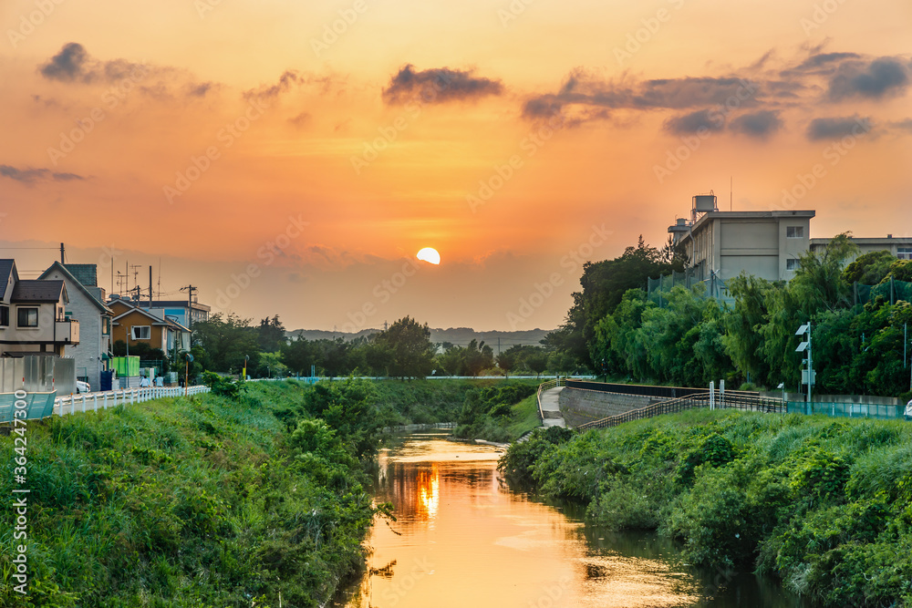 夕日に染まった横浜郊外の鶴見川と夕焼けの太陽