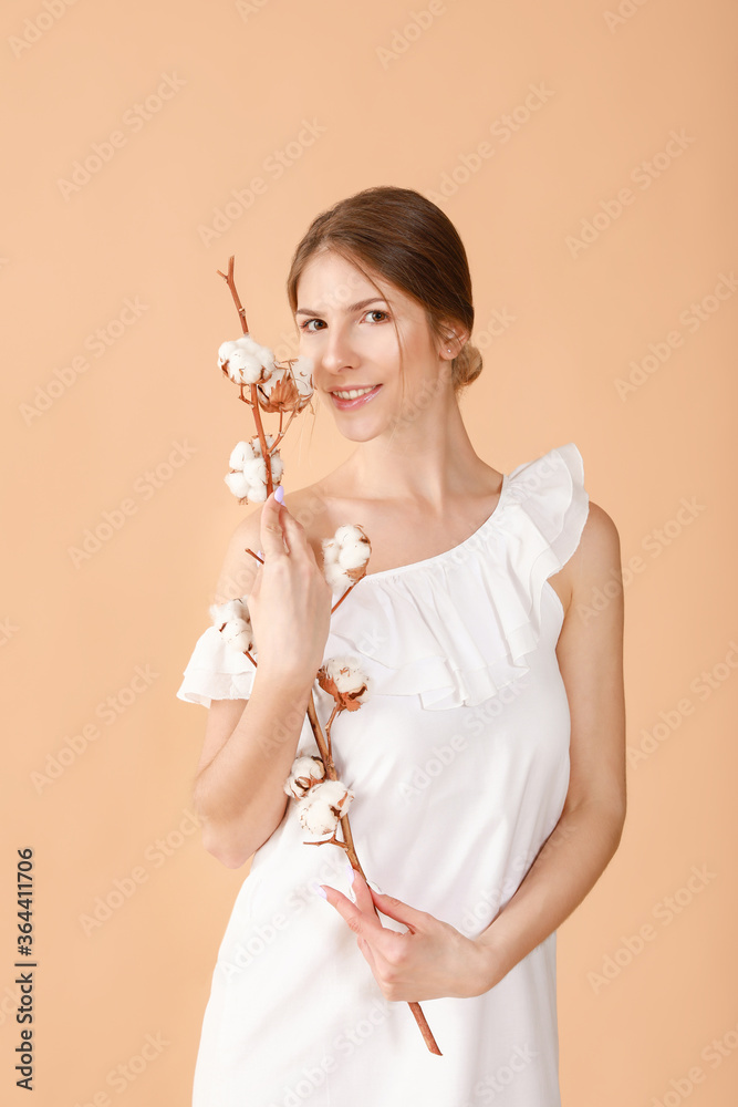 Beautiful young woman with cotton flowers on color background