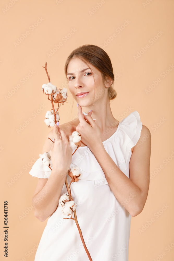 Beautiful young woman with cotton flowers on color background