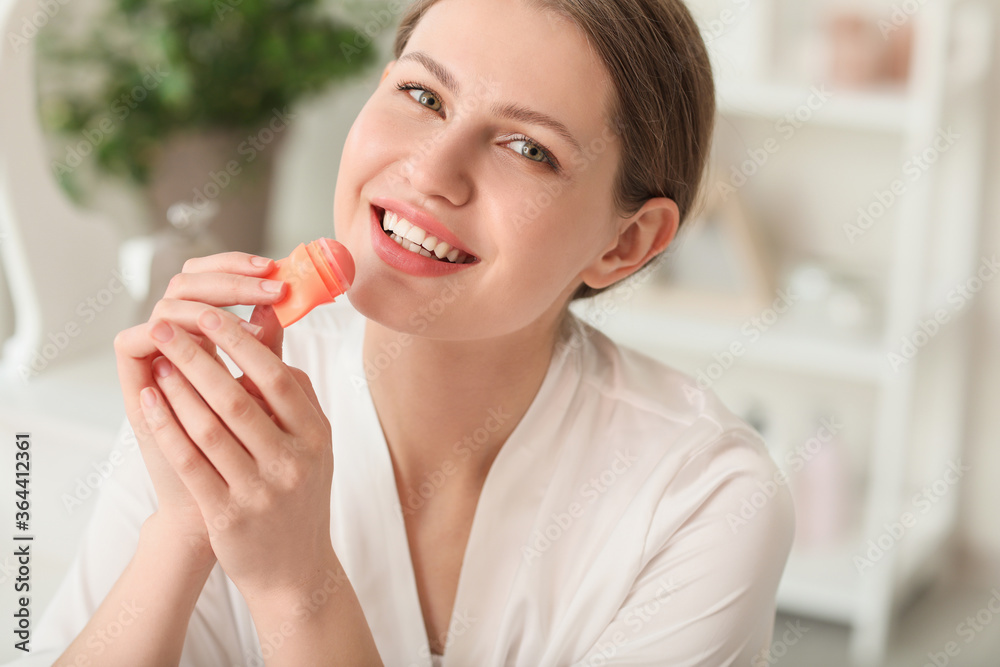 Beautiful young woman with lip balm at home