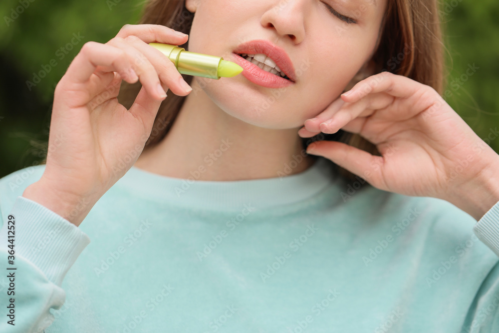 美丽的年轻女人在户外涂润唇膏