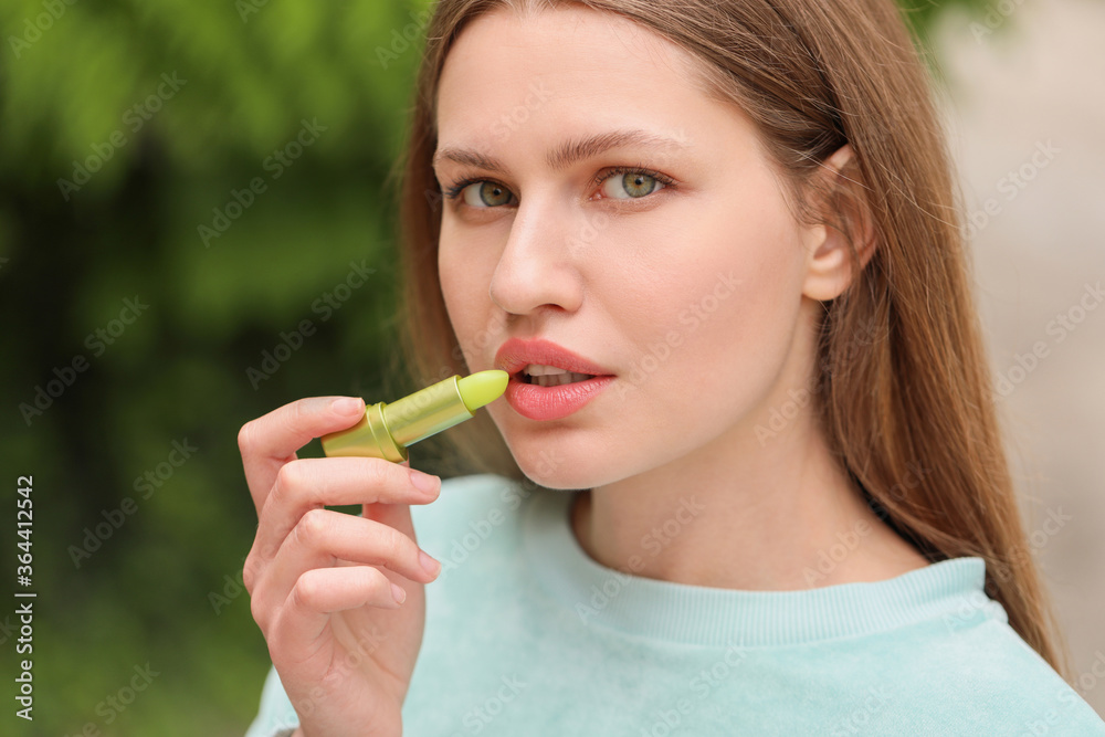 美丽的年轻女人在户外涂润唇膏