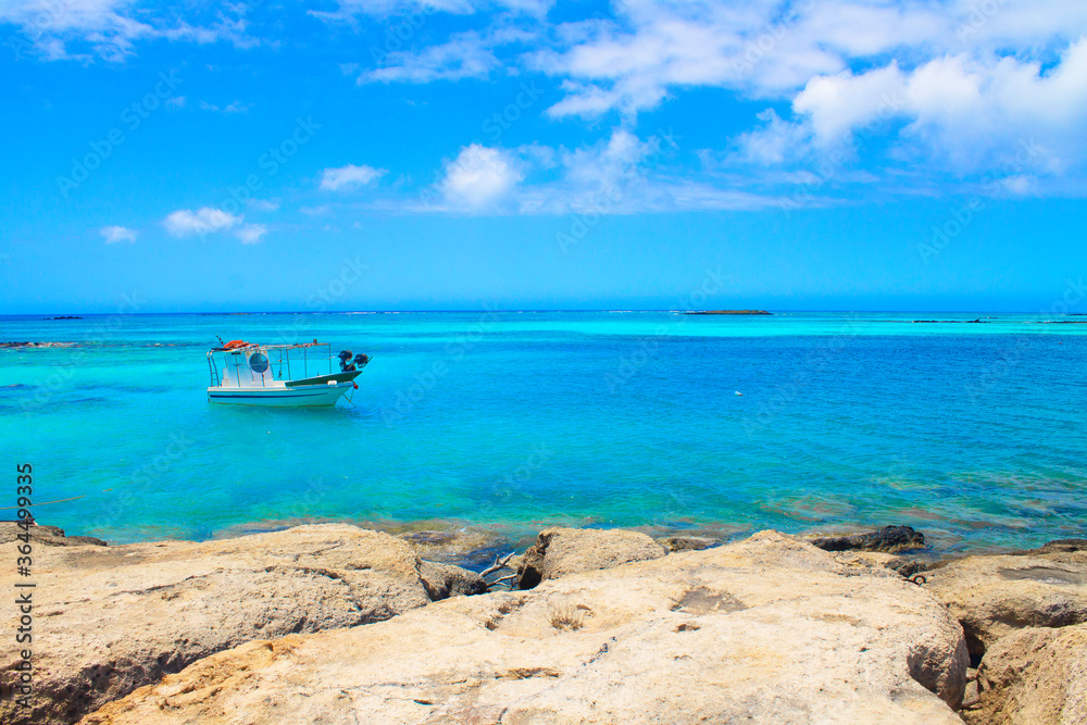 Greece. Crete. 22.06.2020. View of small fish boat, stones, turquoise water and clouds in blue sky.