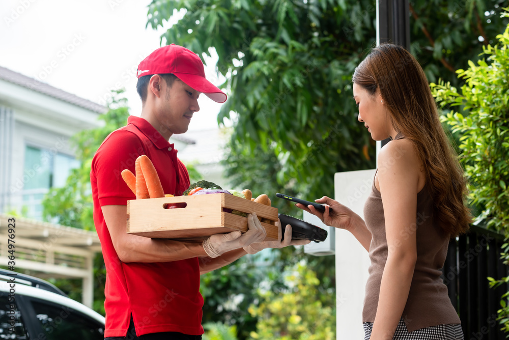 Delivery staff on red uniform holding box of fresh food delivering to customers home and paid by on