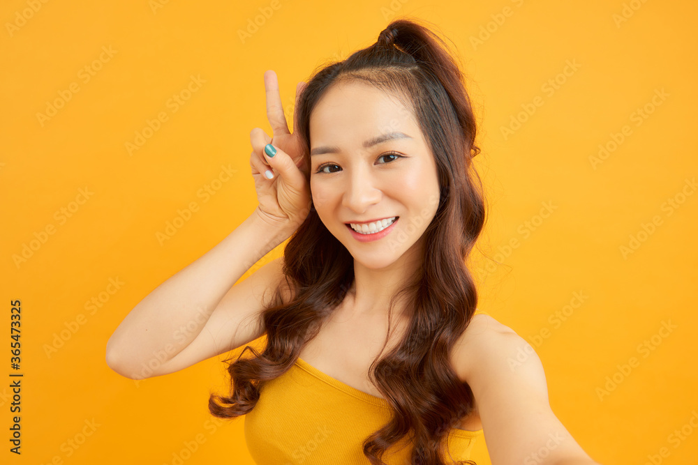 Portrait of beautiful girl selfie in front of camera isolated on orange background. Summer concept