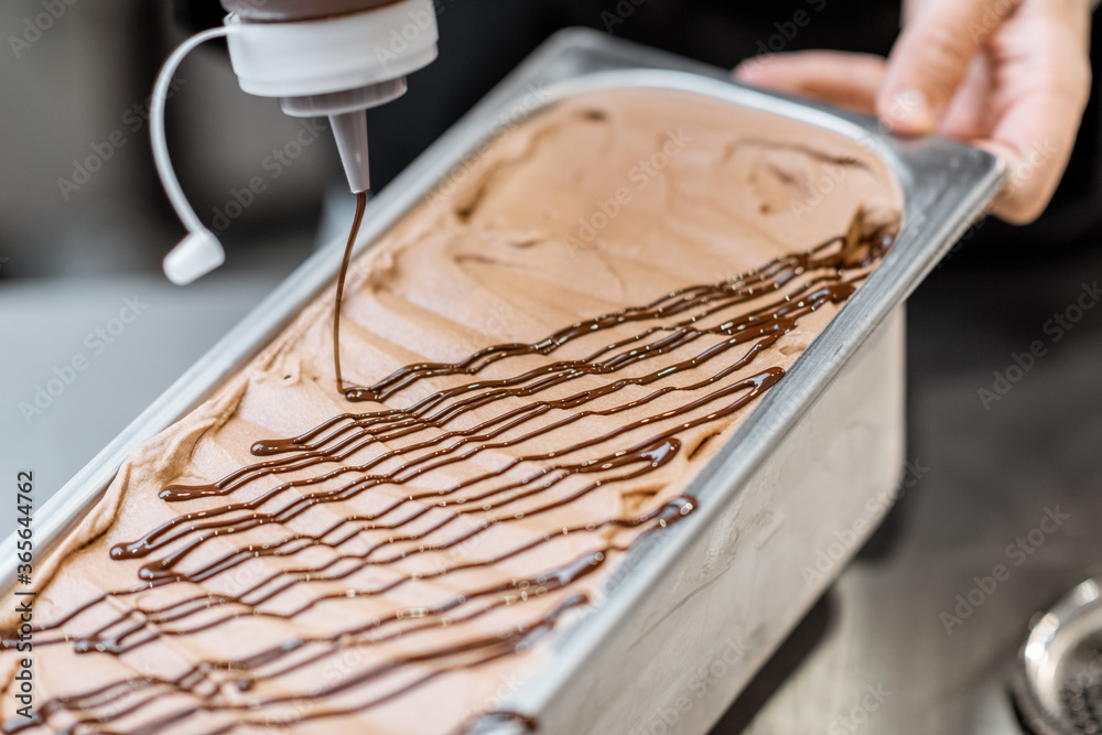 Confectioner pouring chocolate on the ice cream, making ice cream on the kitchen of a small manufact