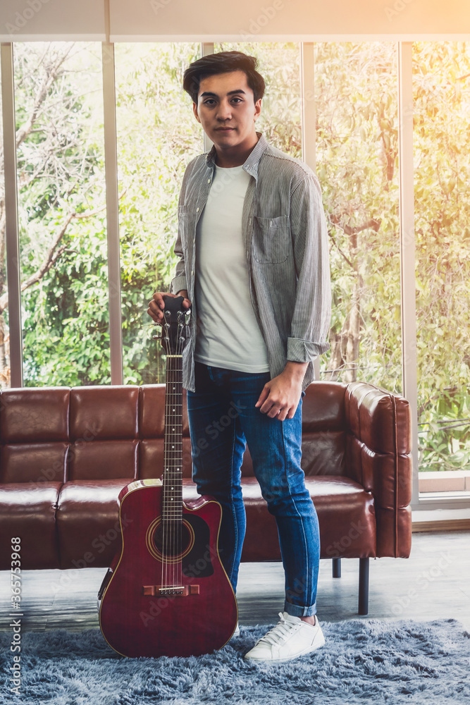 Young guitar player holding his guitar at home. Music and song concept.