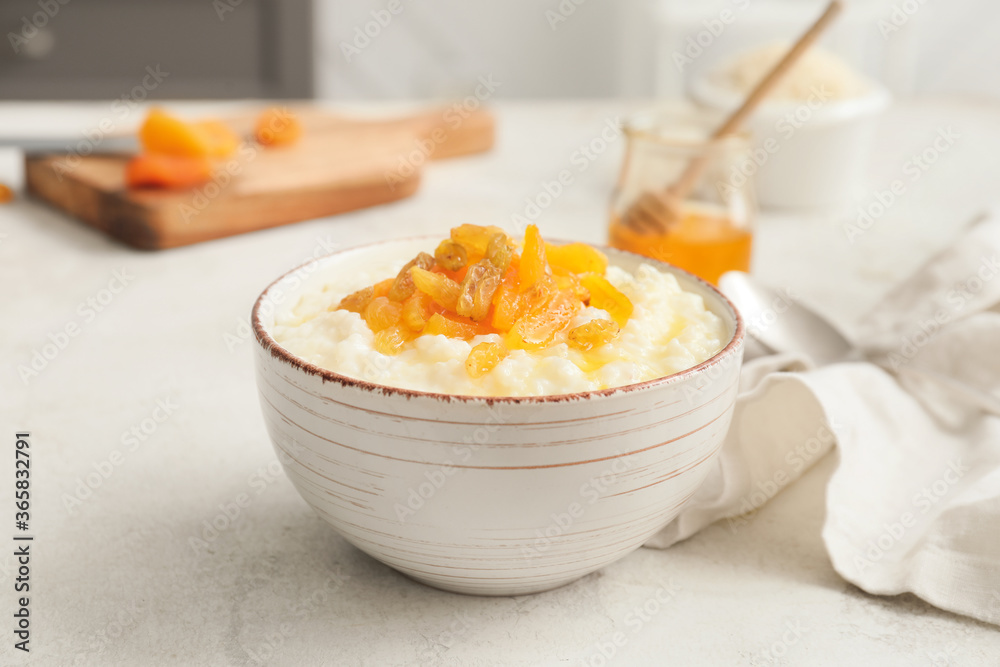 Bowl with boiled rice and fruits on table in kitchen