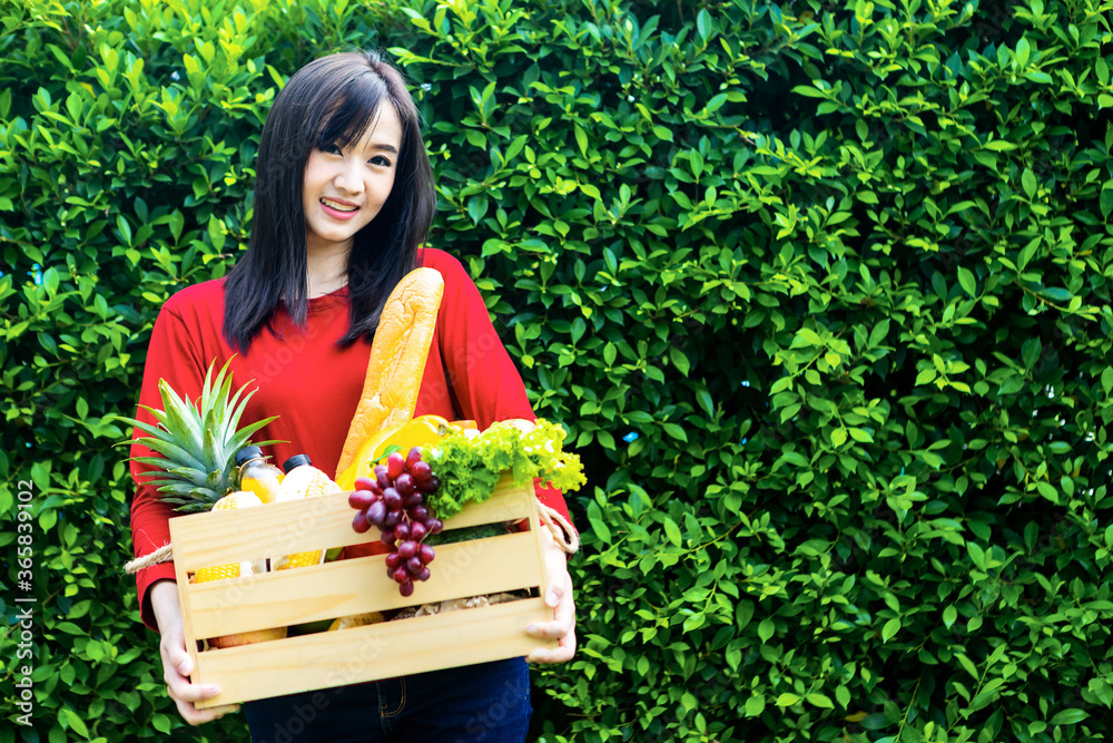 亚洲妇女拿着装有蔬菜的木篮子。篮子里有新鲜蔬菜。在花园野餐