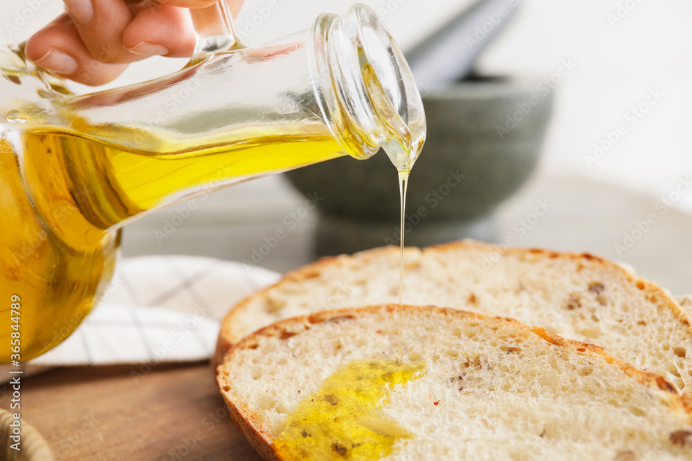 Woman pouring tasty olive oil onto bread slice, closeup