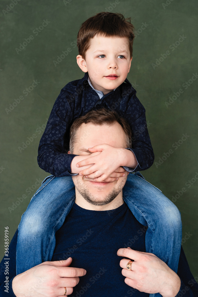 boy is sitting on his fatherТs shoulders, covers dadТs face with his hands