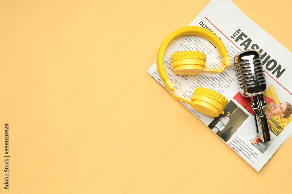 Headphones with microphone and newspaper on color background