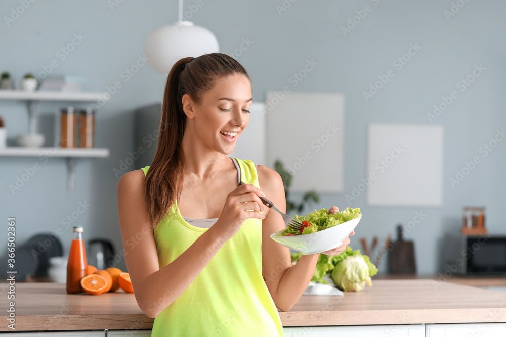 漂亮的年轻女人在厨房吃蔬菜沙拉