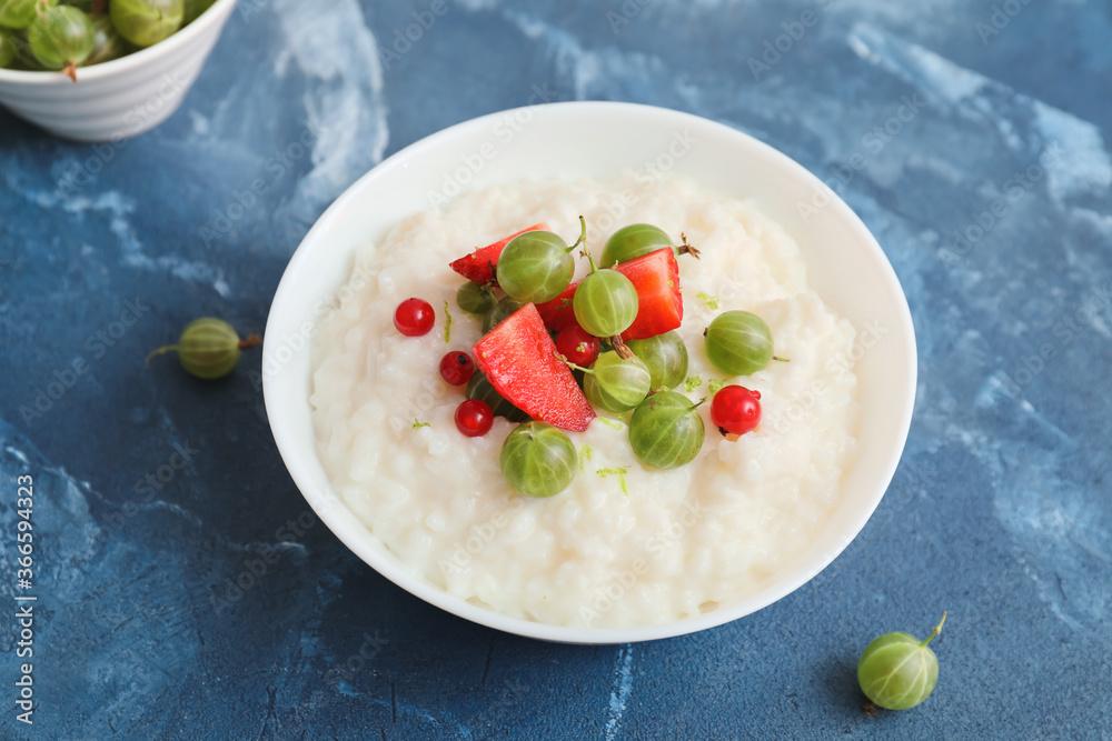 Bowl with boiled rice and berries on color background