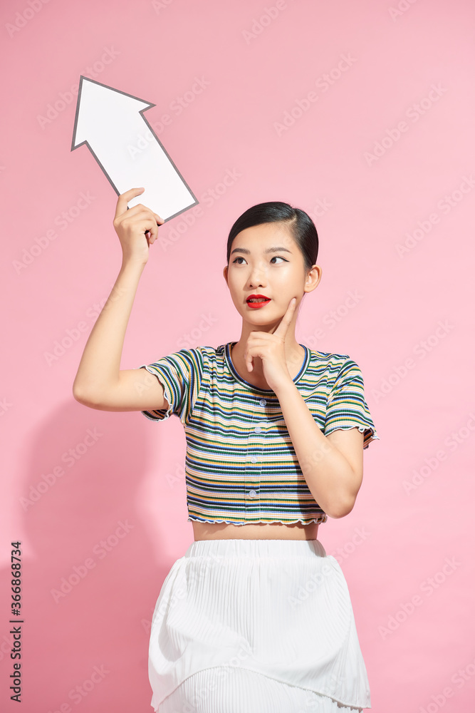 Portrait of an excited young african woman pointing away with a paper arrow isolated over pink backg