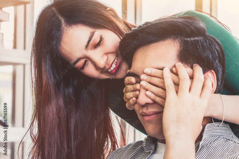 Happy Asian couple play covering eyes in living room.