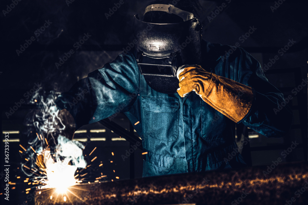 Metal welder working with arc welding machine to weld steel at factory while wearing safety equipmen