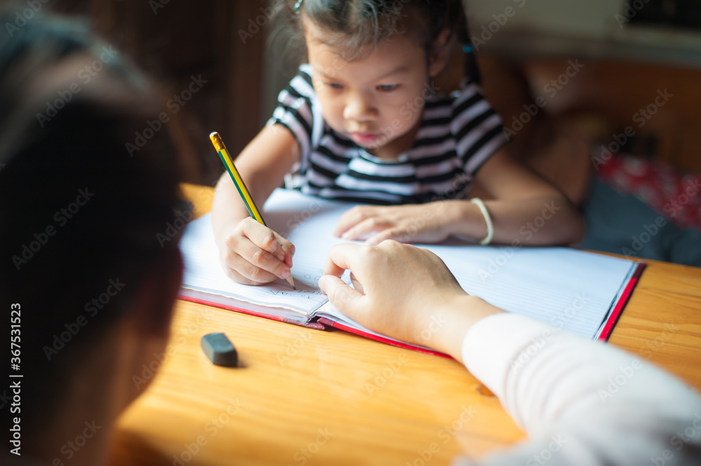 Mother helped his four-year-old daughter do homework. The little girl is serious about writing pract