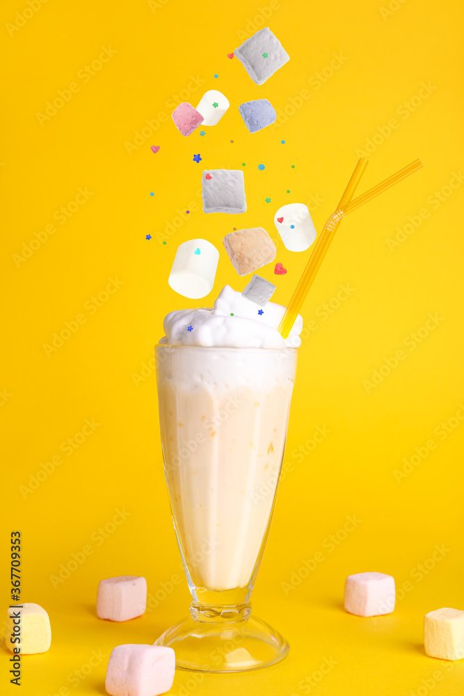 Glass of tasty milkshake and falling ingredients on color background