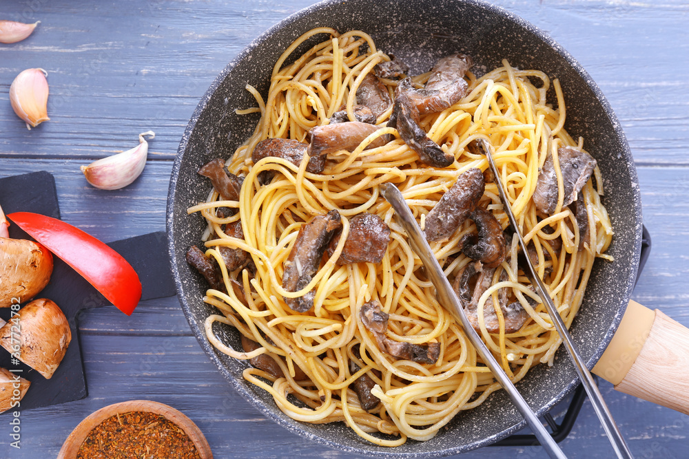 Frying pan with tasty pasta and mushrooms on table