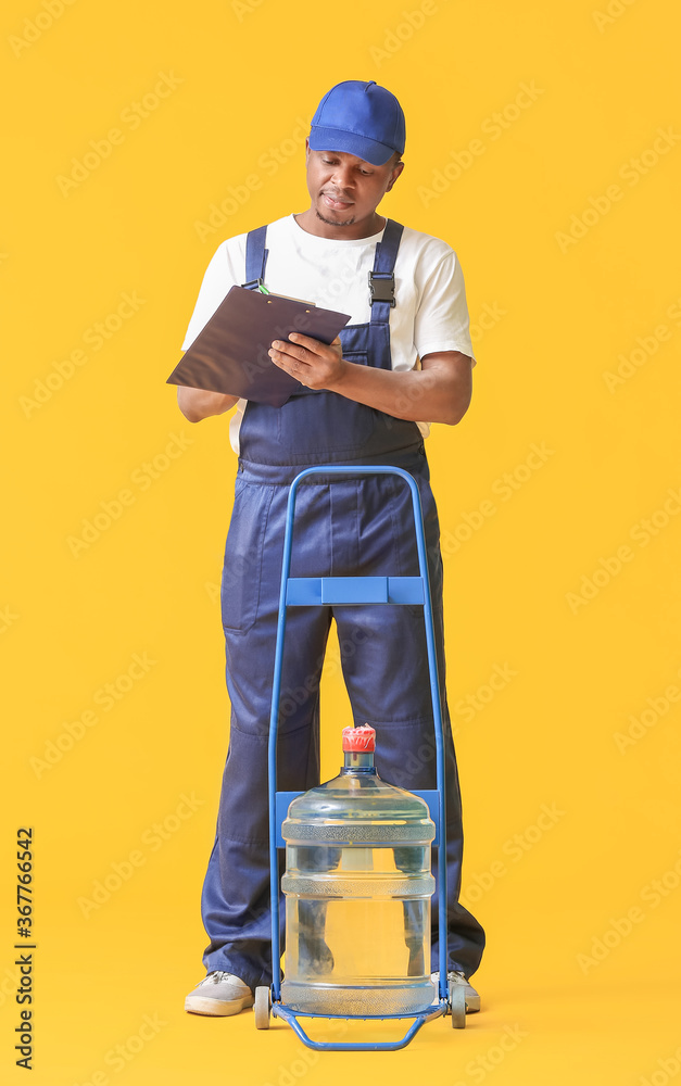 African-American delivery man with bottle of water on color background