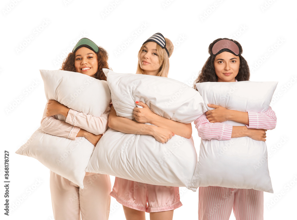 Beautiful young women in pajamas and with pillows on white background