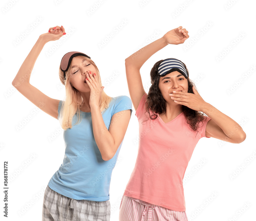 Beautiful young women in pajamas and with sleep masks on white background