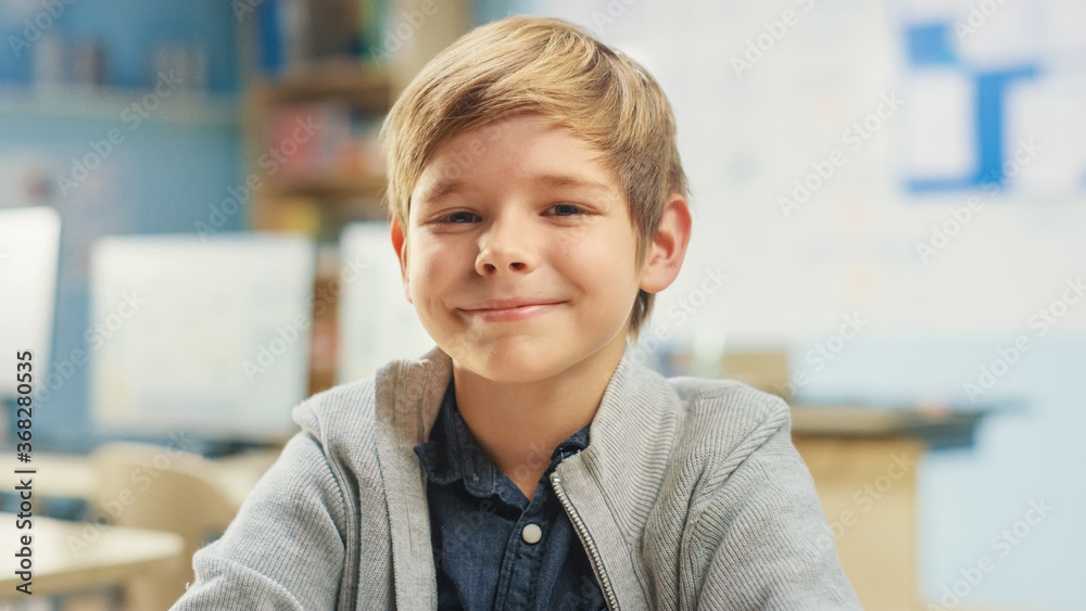 一个可爱的小男孩坐在学校的桌子旁，开心地笑着。聪明的炭色小男孩的画像