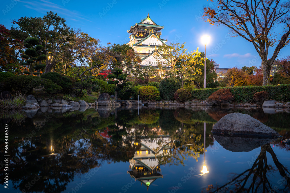 日本大阪，秋季夜晚，带日本花园和池塘倒影的大阪城堡。